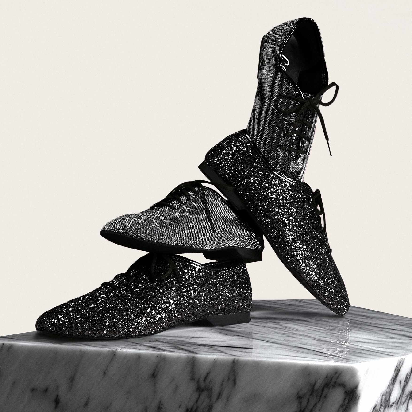 Glitzernde schwarze Schnürschuhe, gestapelt auf einer Marmoroberfläche vor hellem Hintergrund.